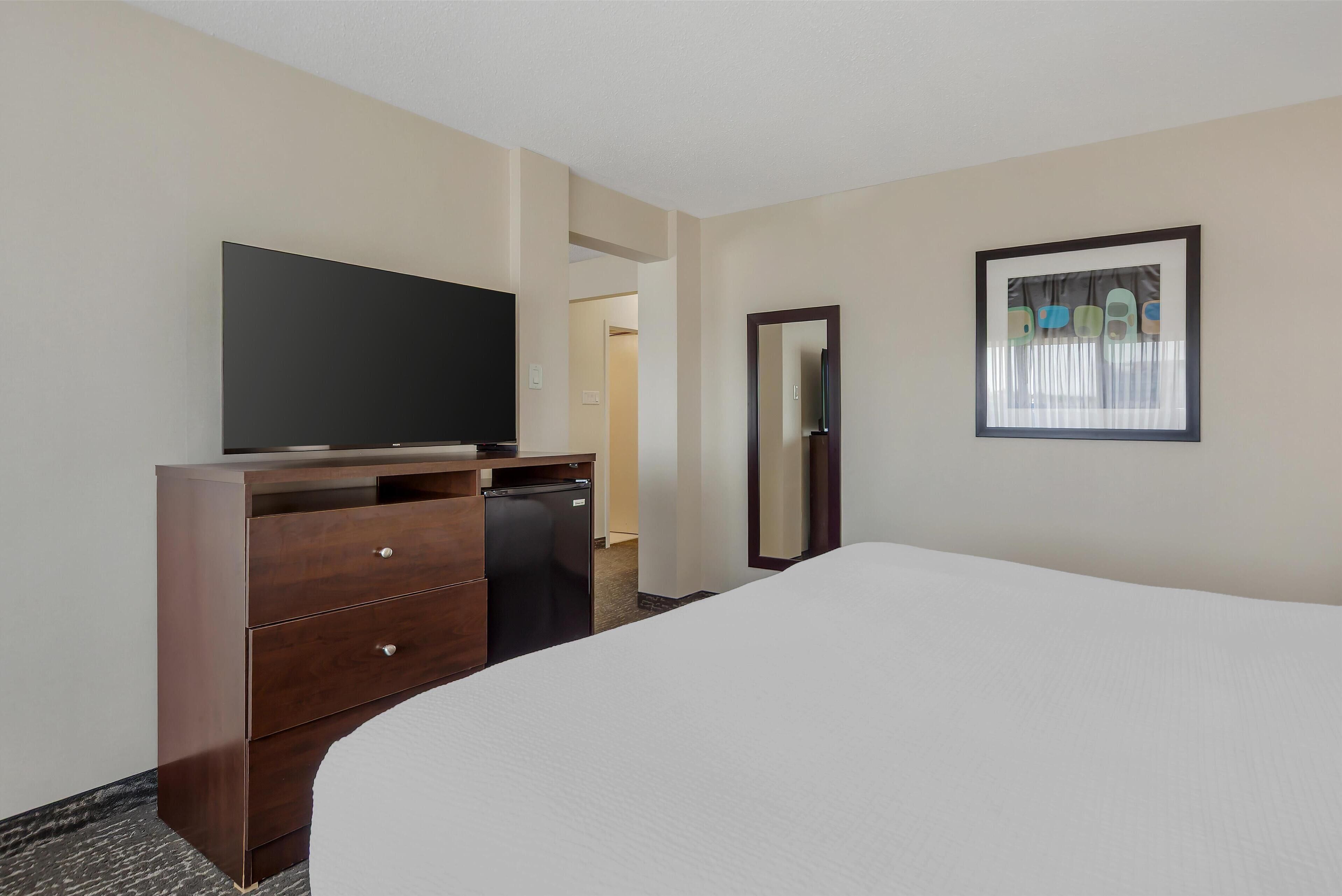 A hotel room with a bed, a dresser, a television, and a mirror.