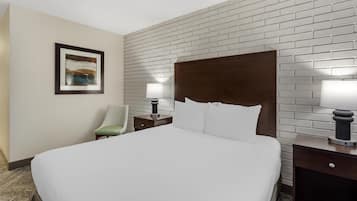A hotel room with a large bed, a nightstand with a lamp, a chair, and a framed picture on the wall.