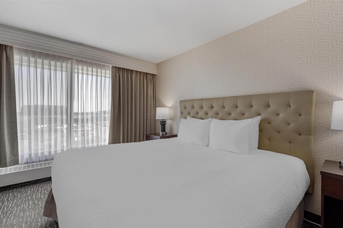 A hotel room with a large bed, a nightstand with a lamp, and a window with curtains.