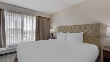 A hotel room with a large bed, a nightstand with a lamp, and a window with curtains.