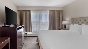 A hotel room with a large bed, a television on a dresser, a desk, and a window with curtains.