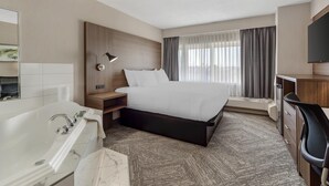 A modern hotel room with a large bed, a separate desk area, a bathtub, and a large window with curtains. - Best Western Cedar Park Inn (Edmonton)