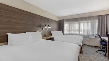 A hotel room with two beds, a desk, a chair, and a window with curtains.