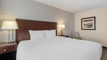 Habitación de hotel con una cama grande, dos lámparas de noche, un cabecero de madera, una mesita de noche, una silla y un cuadro en la pared.