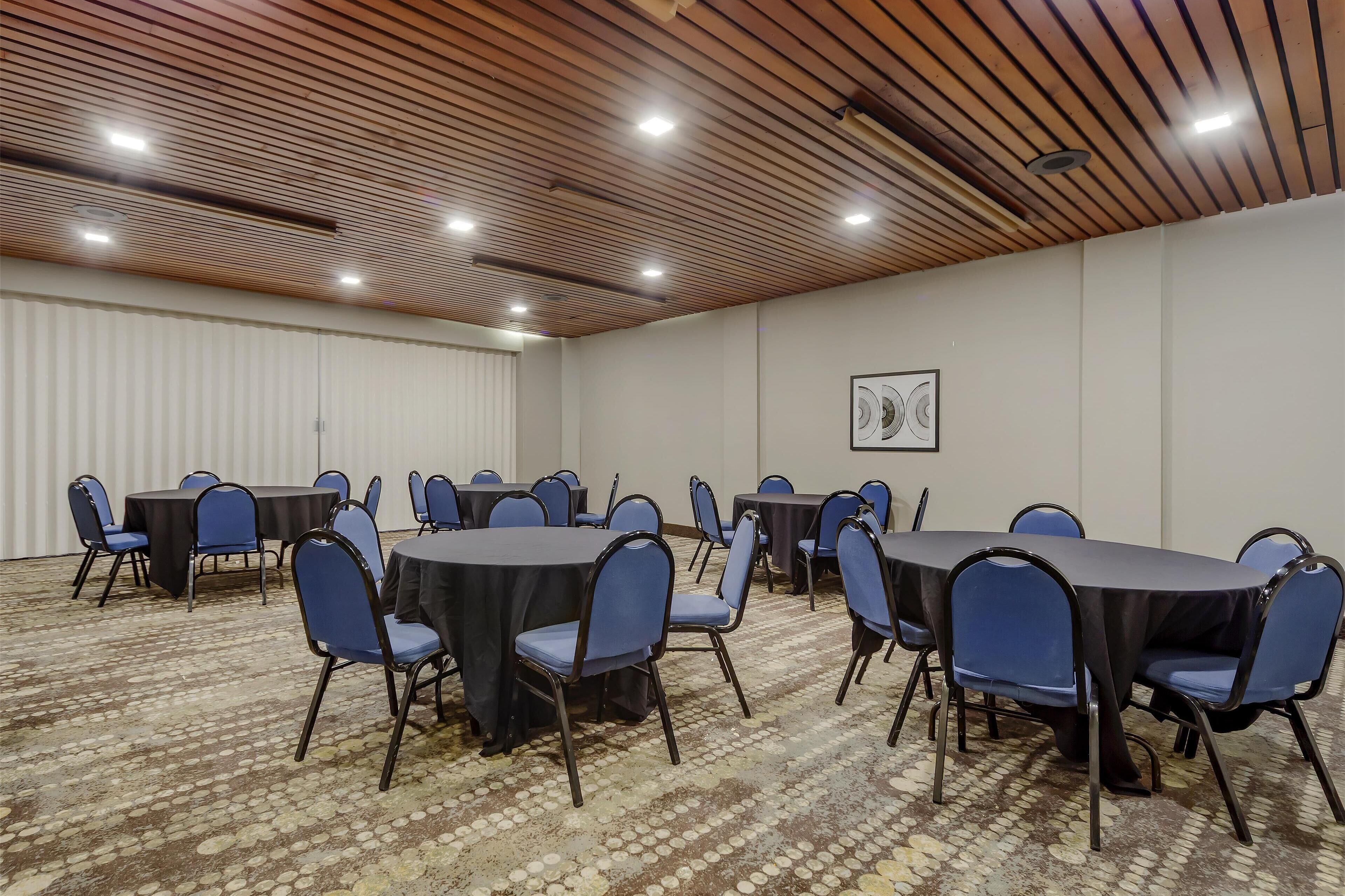 Un salón de conferencias con mesas redondas y sillas azules, techo de madera y alfombra estampada.
