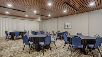 Un salón de conferencias con mesas redondas y sillas azules, techo de madera y alfombra estampada.