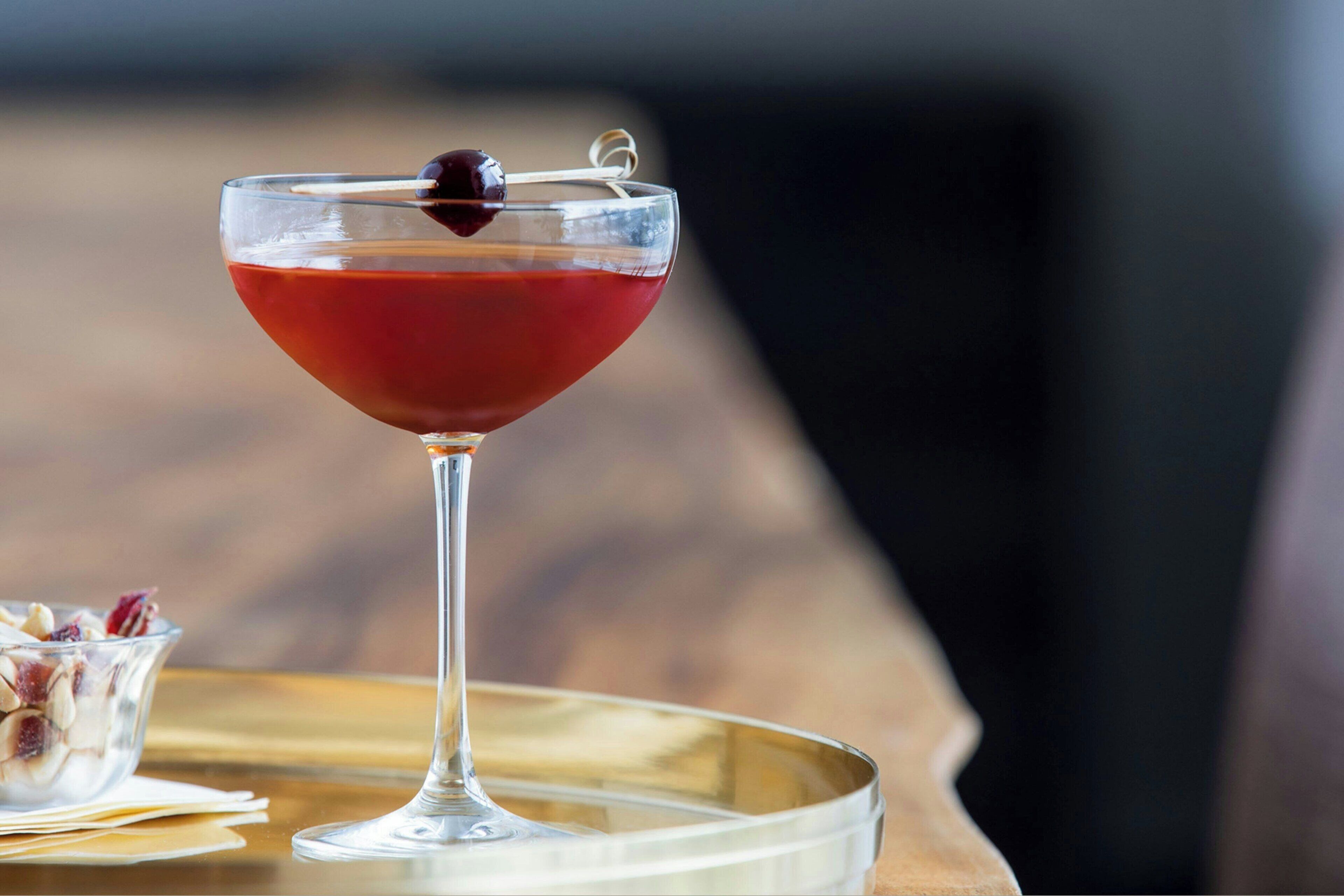 A martini glass with a cherry on a cocktail tray.