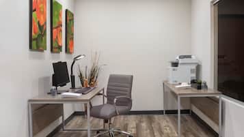 An office with two desks, one with a computer and keyboard, and the other with a printer and a plant.