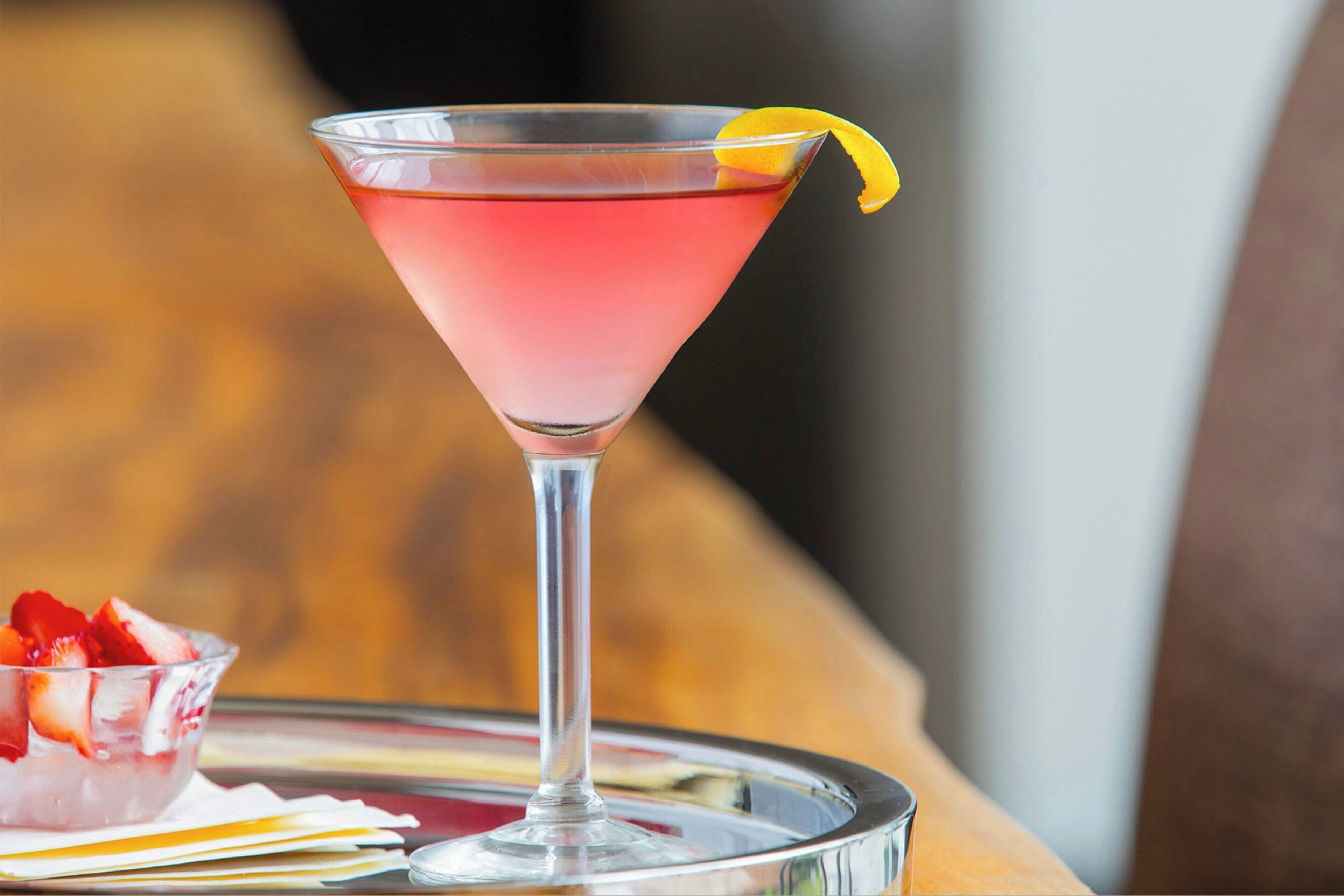 Ein Cocktail im Martini-Glas mit Zitronenzeste, platziert auf einer Platte mit Erdbeeren.