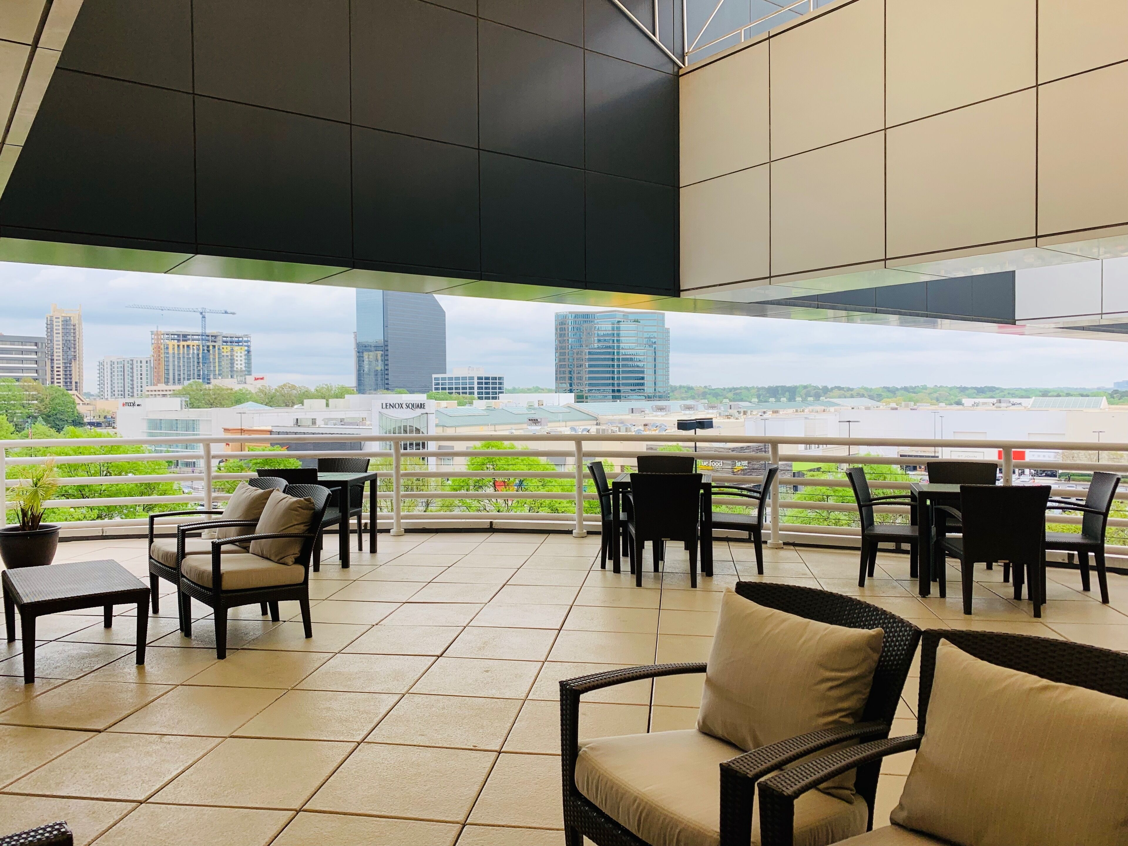 A terrace with outdoor seating, a view of city buildings, and a railing.
