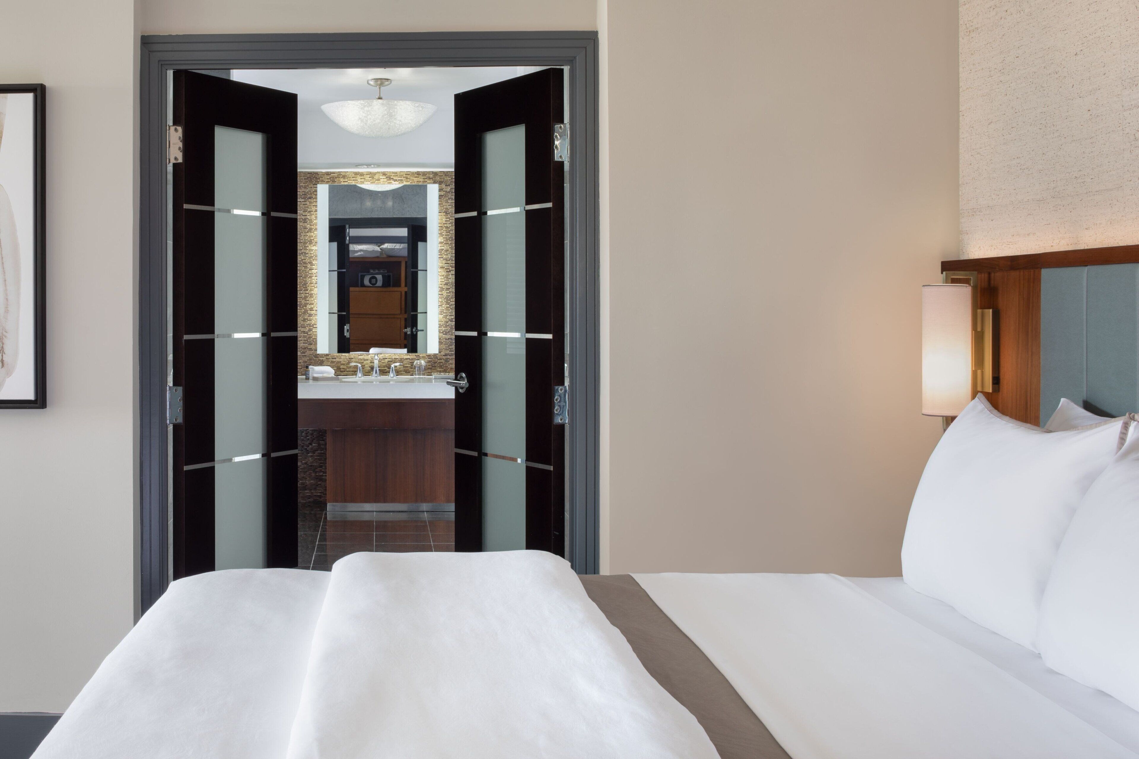 A hotel room with a large bed, a bathroom with a mirror, and a wooden cabinet.