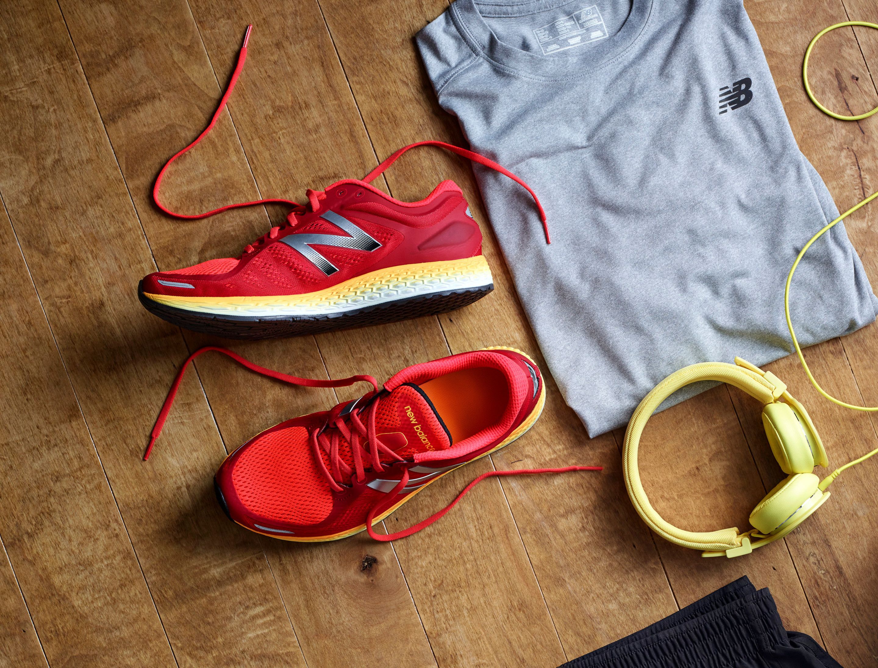 Un par de zapatillas rojas para correr, una camiseta gris y auriculares amarillos sobre un suelo de madera.