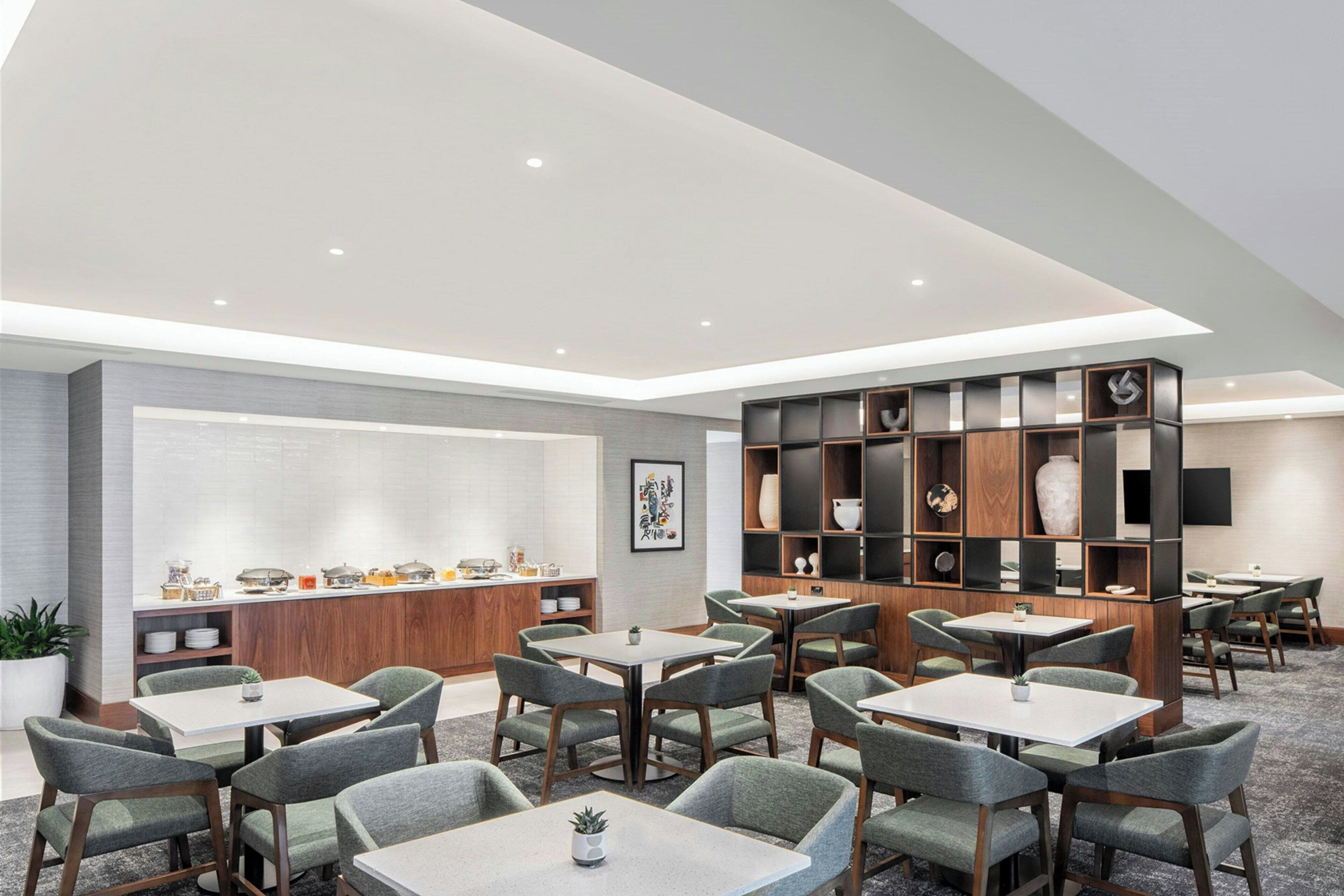 A modern hotel lobby with multiple seating areas, a reception desk, and a decorative bookshelf.