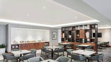A modern hotel lobby with multiple seating areas, a reception desk, and a decorative bookshelf.