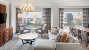 A modern hotel room with a large window, a chandelier, a flat-screen TV, a sofa, a dining table, and a wooden cabinet. - The Westin Buckhead Atlanta (Atlanta)