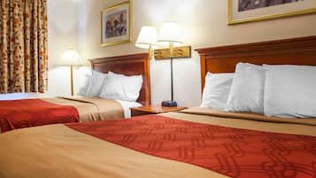 A hotel room with two beds, each with a red and beige bedspread, a wooden headboard, and a nightstand with a lamp.