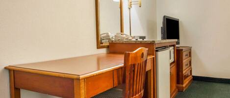 A hotel room with a wooden desk, a chair, a television, a telephone, and a mirror.