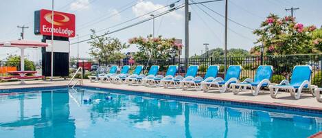 A swimming pool with blue lounge chairs and a red sign for EconoLodge.