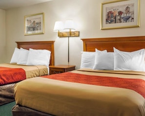 A hotel room with two beds, each with white linens and a red patterned bedspread. There is a nightstand with a lamp between the beds, and two framed pictures on the walls.