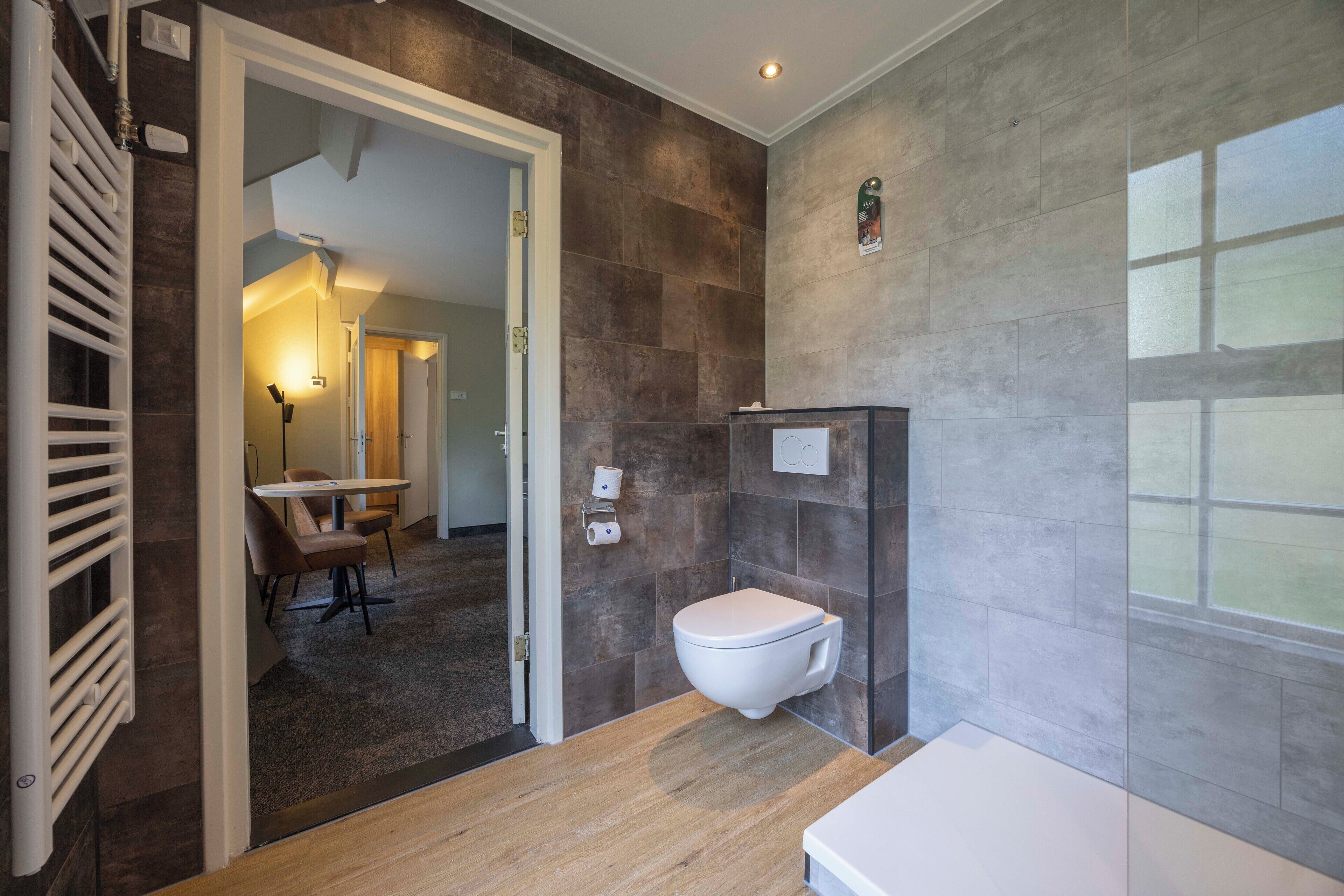 Un baño moderno con inodoro, ducha y lavamanos. El suelo es de madera y hay un radiador fijado a la pared.