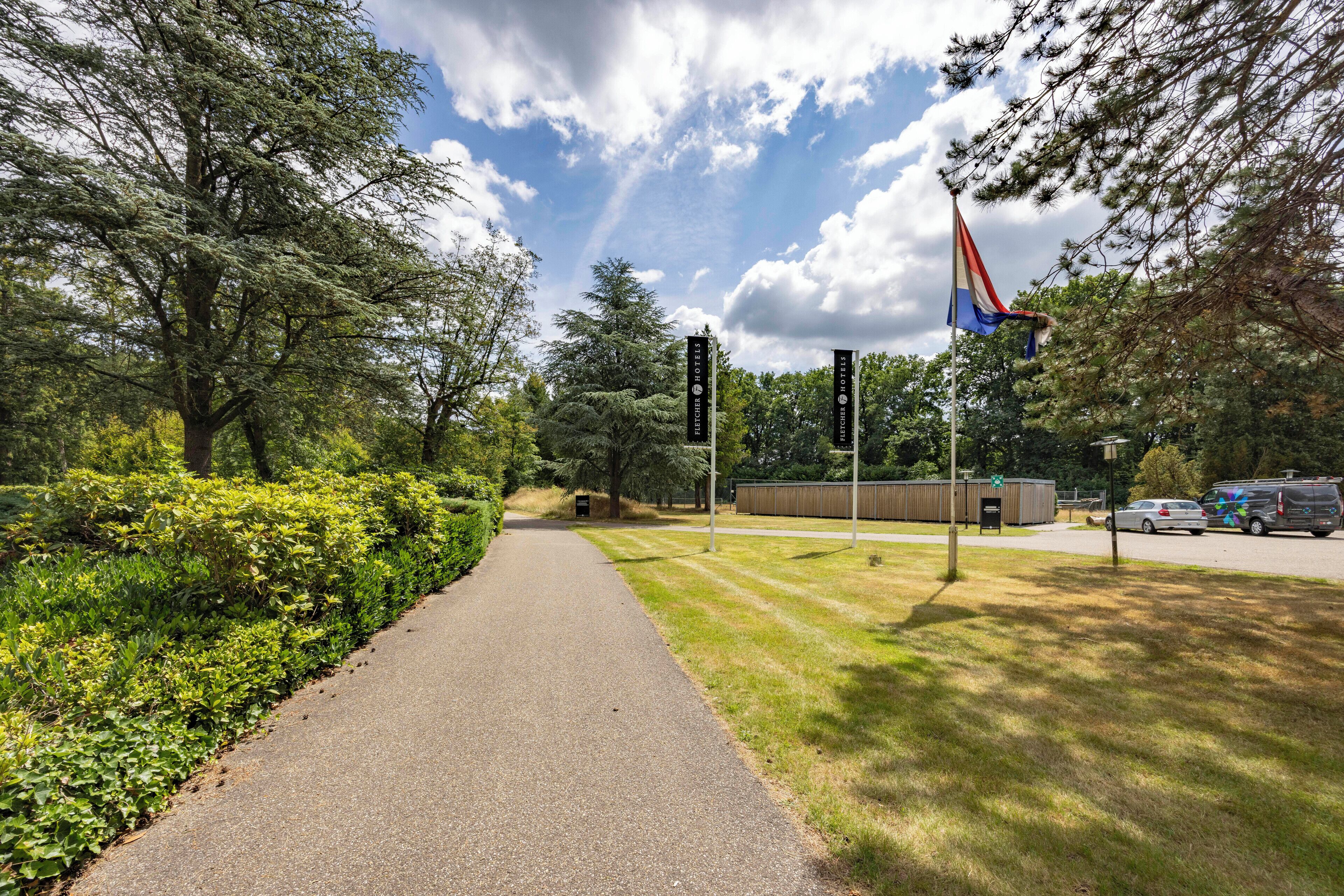 A pathway leading to a building with flags and signs, surrounded by trees and greenery.