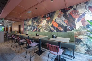 A modern restaurant with a large abstract mural, wooden tables, and cushioned seating.