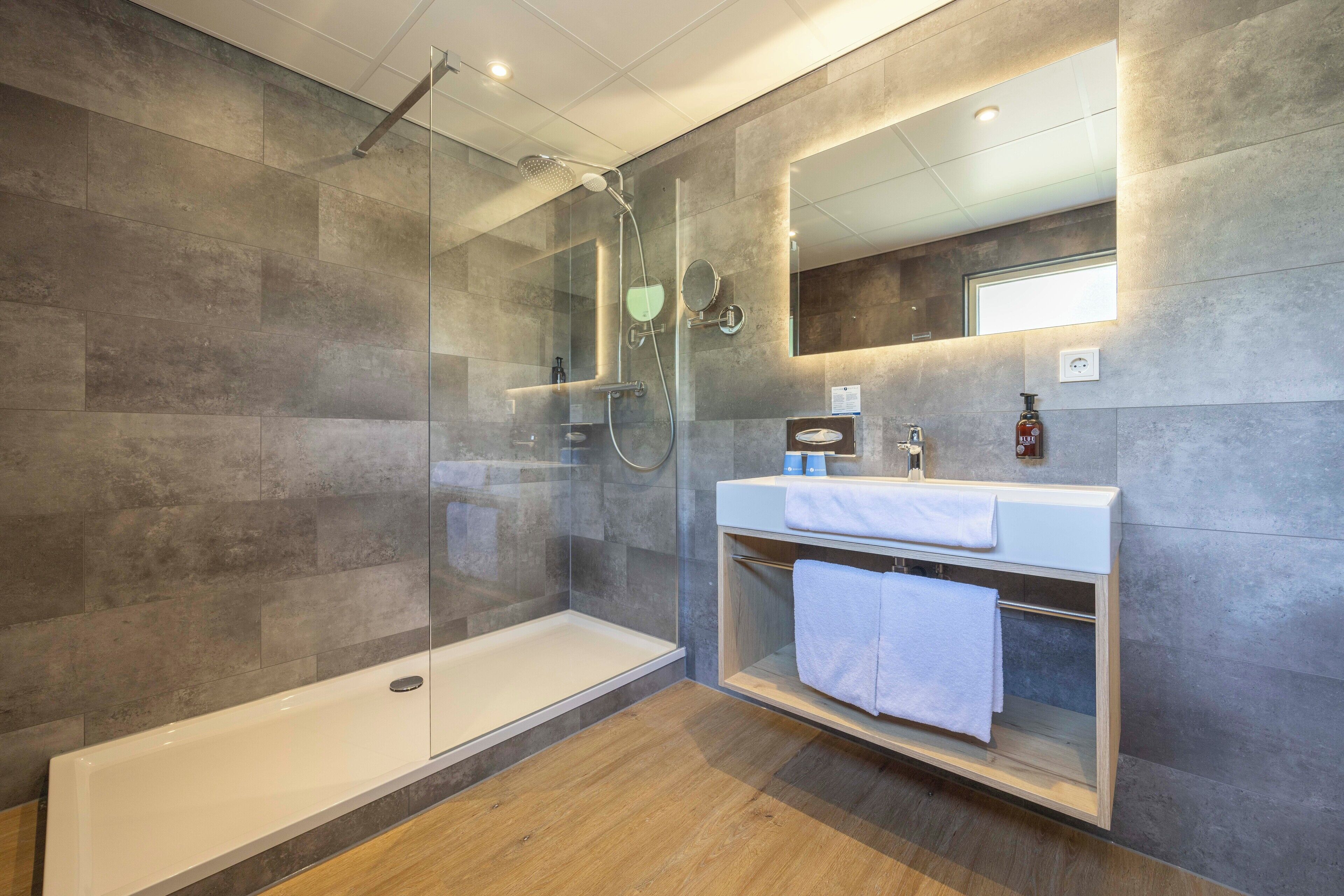Une salle de bain moderne dotée d’une douche à parois de verre, d’une baignoire blanche et d’un meuble-lavabo avec un miroir et un porte-serviettes.