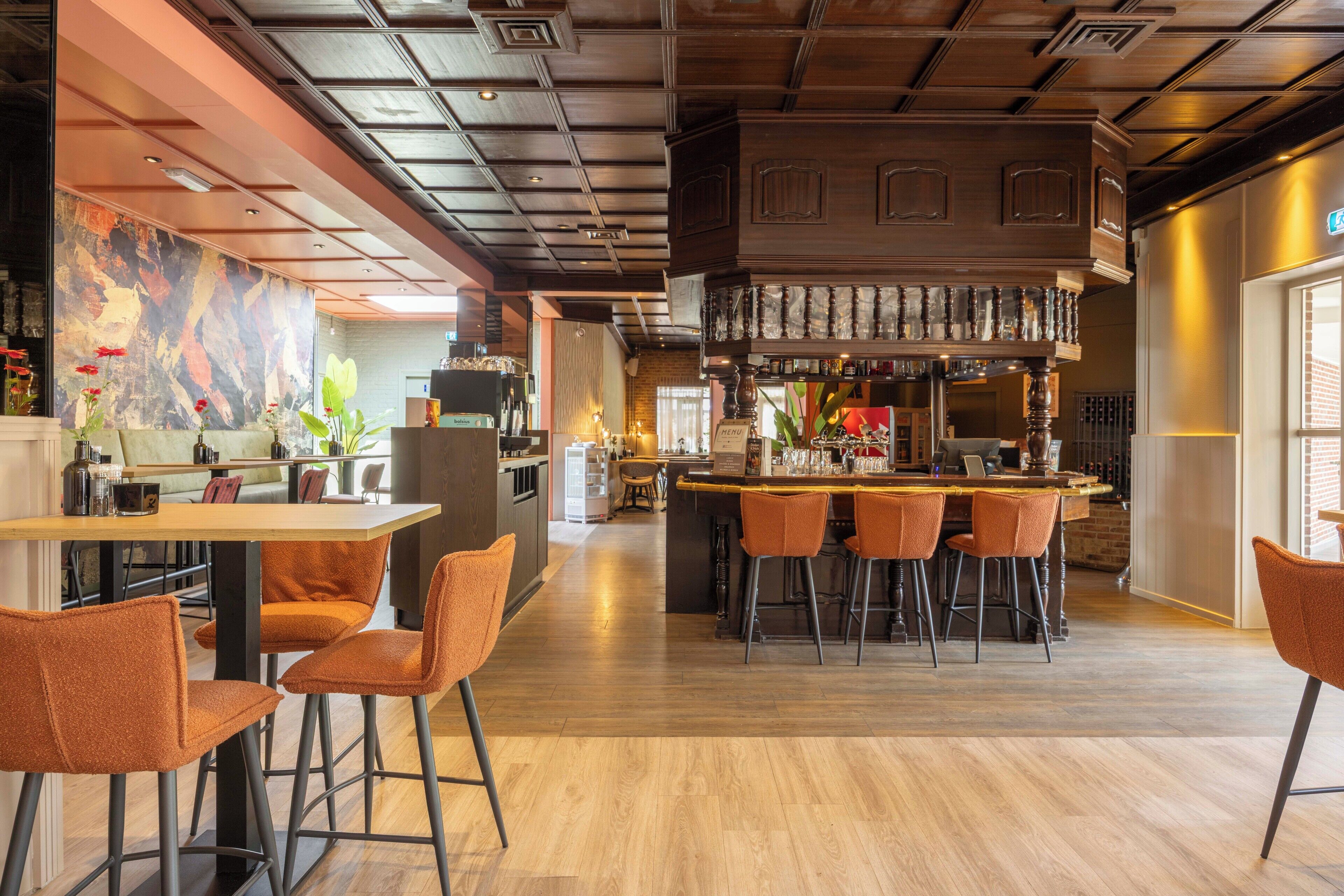 Een moderne bar met een houten toog, barstoelen en een zithoek met tafels en stoelen.