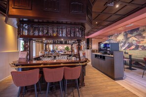A bar area with a wooden bar counter, multiple stools, and a variety of bottles and glasses. - Fletcher Hotel - Restaurant Victoria - Hoenderloo (Hoenderloo)