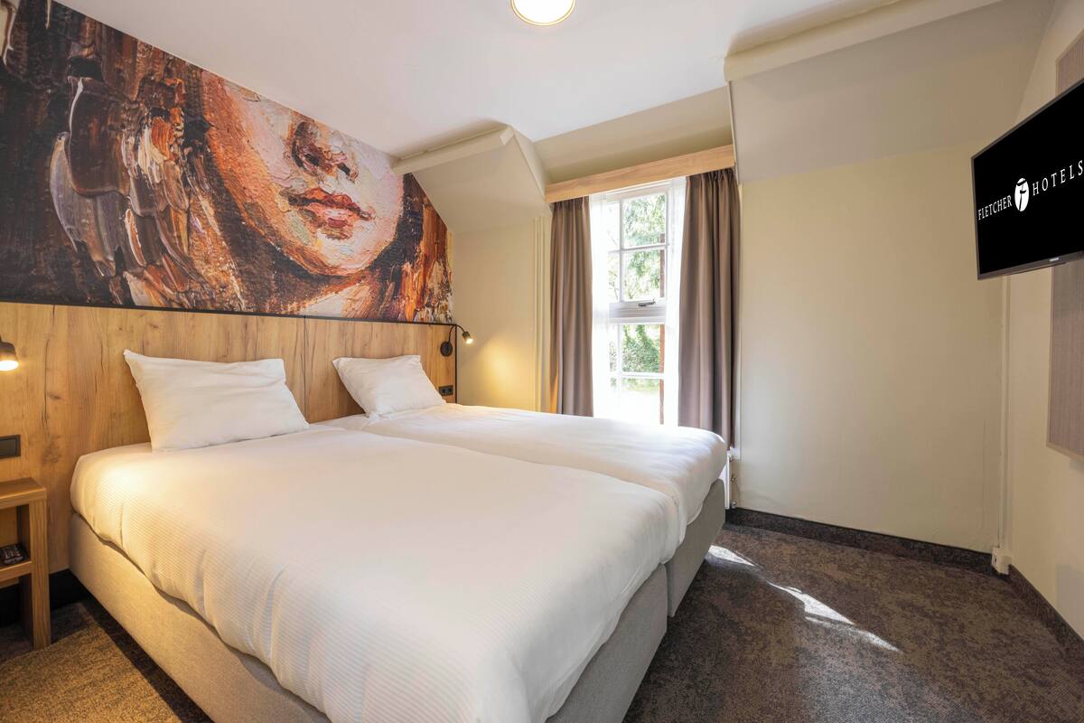 A hotel room with a large bed, a wooden headboard, a painting on the wall, a television, and a window with curtains.