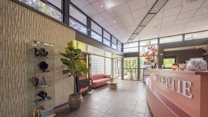 A modern reception area with a glass display of jewelry, a seating area with a pink sofa, and a reception desk labeled "RECEPTION". - Fletcher Hotel - Restaurant Victoria - Hoenderloo (Hoenderloo)