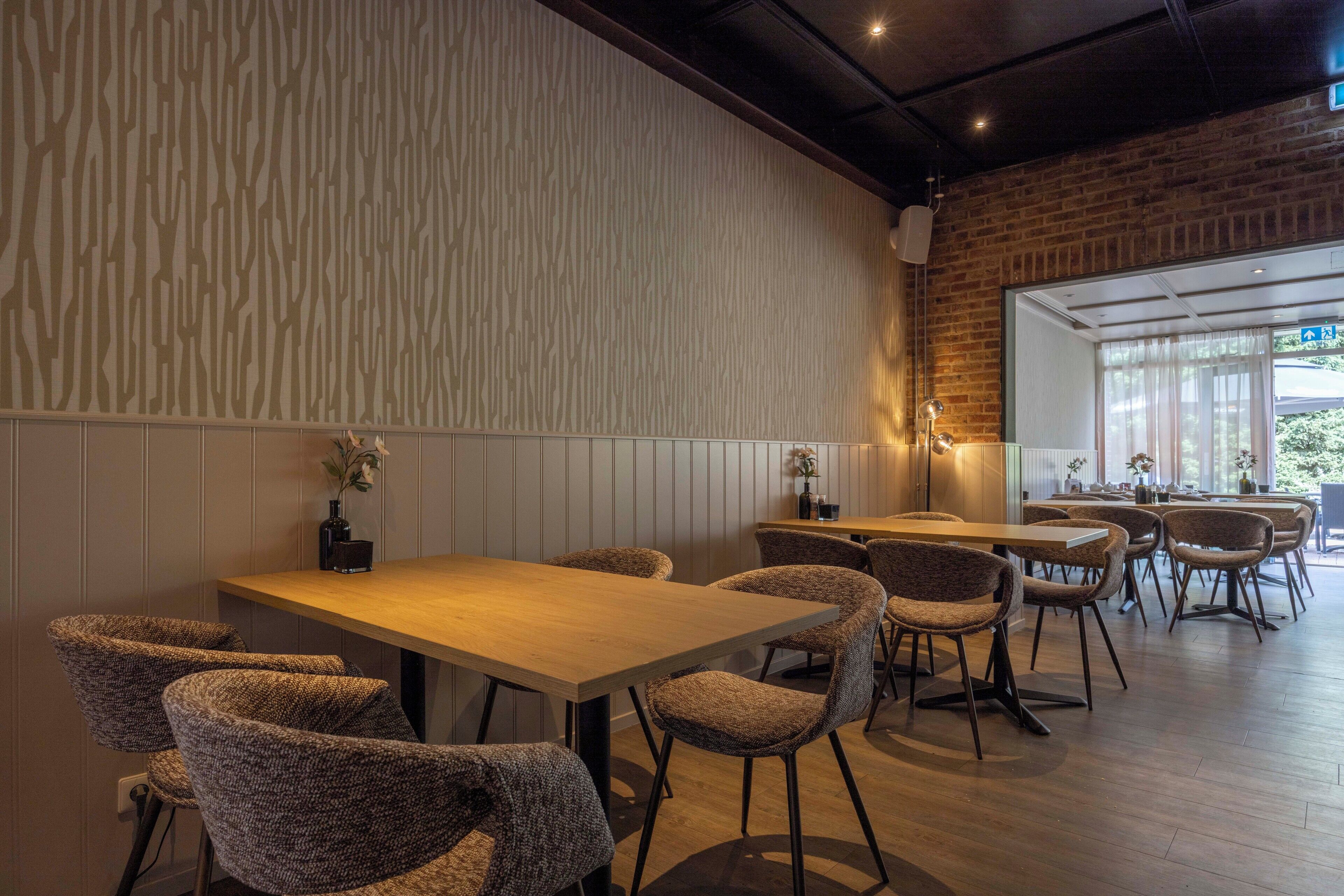 Un restaurant amb taules i caires de fusta, una paret de rajola i un gran finestral.