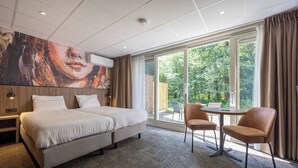 A modern hotel room with a large bed, two chairs, a small table, and a large window with a view of greenery. - Fletcher Hotel - Restaurant Victoria - Hoenderloo (Hoenderloo)