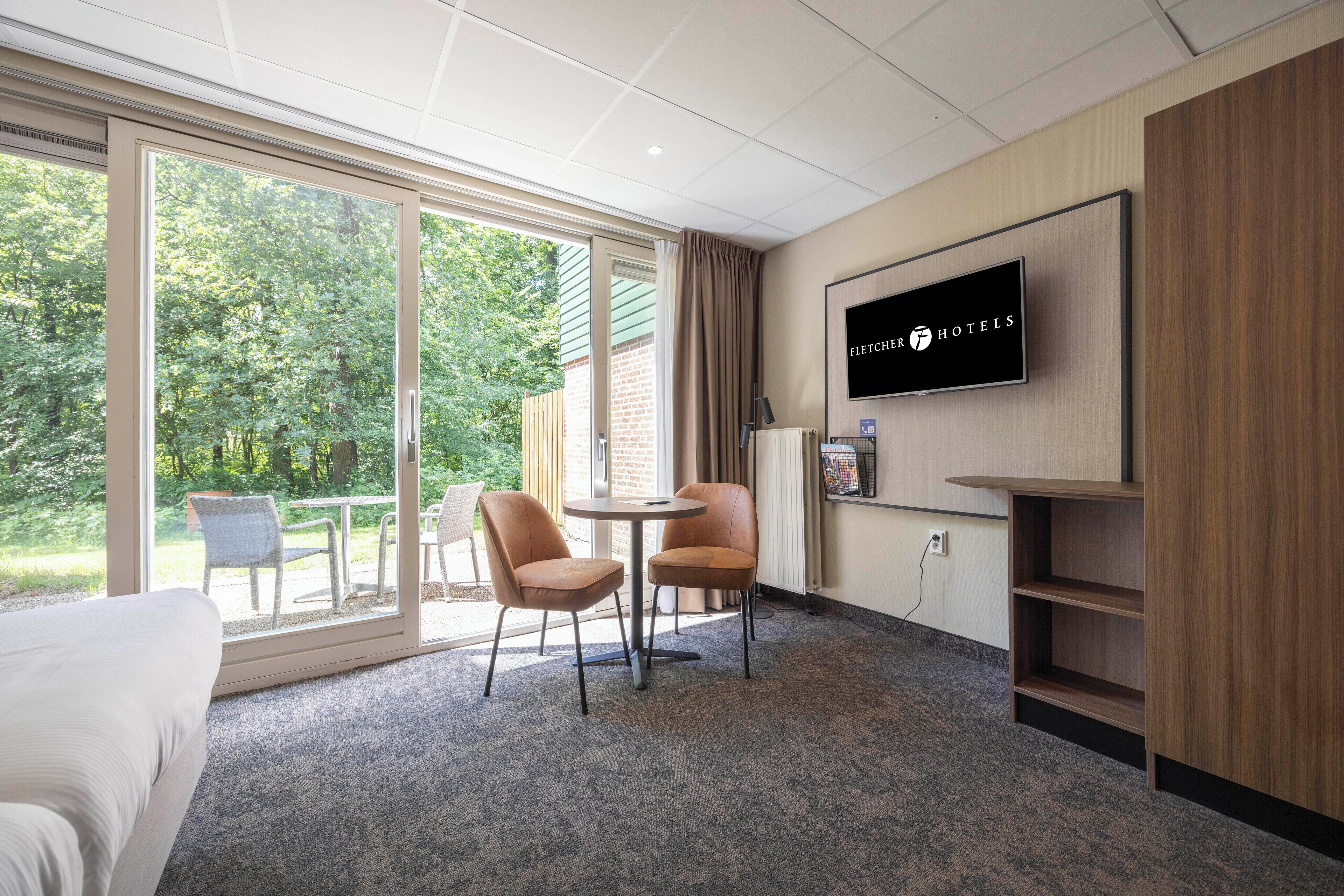A hotel room with a large window, a bed, a TV, and a seating area with chairs and a table.
