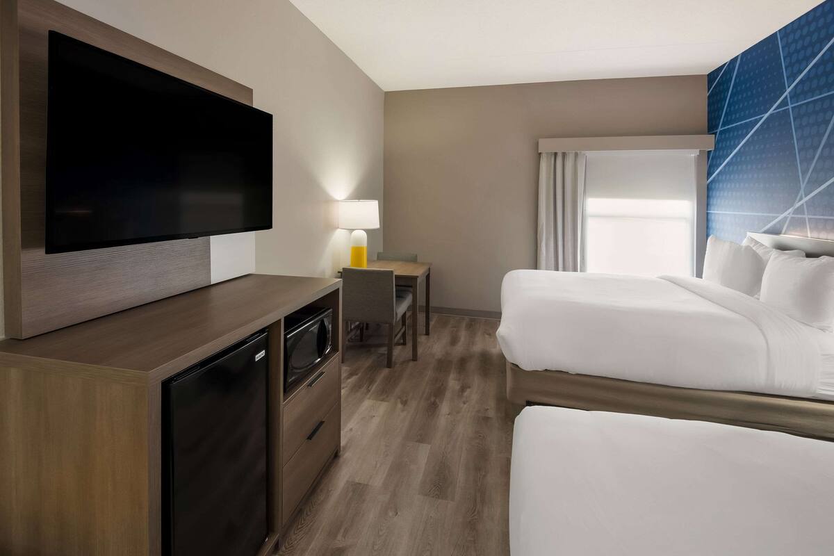 Habitación de hotel con televisión de pantalla plana, escritorio con lámpara, dos camas y ventana con cortinas.
