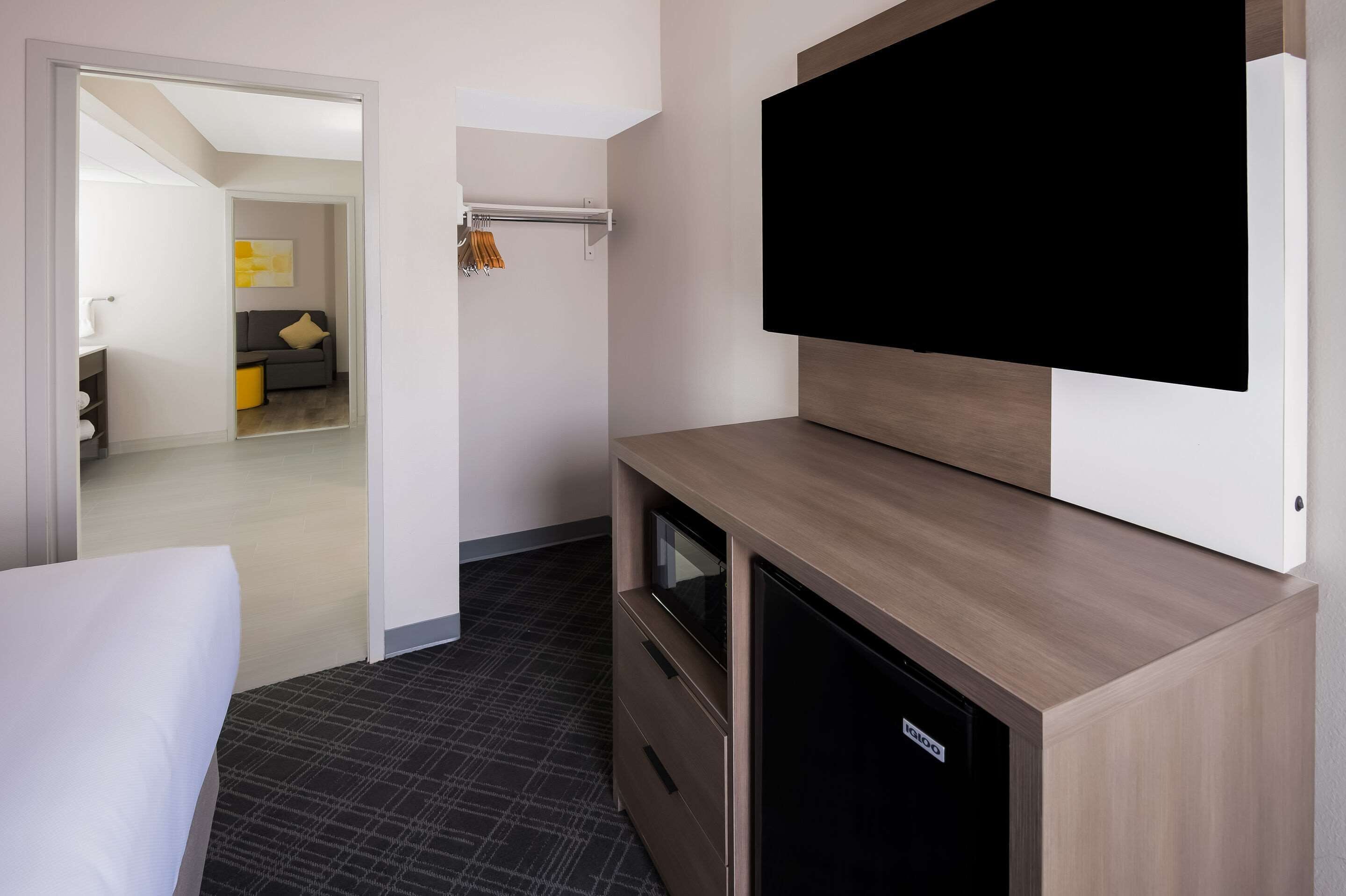 Una habitación de hotel con una cama, un televisor montado en la pared, un armario de madera y un pequeño escritorio.