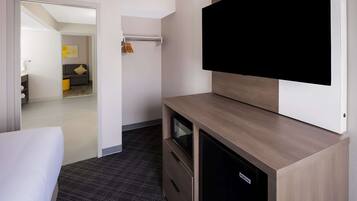 Una habitación de hotel con una cama, un televisor montado en la pared, un armario de madera y un pequeño escritorio.