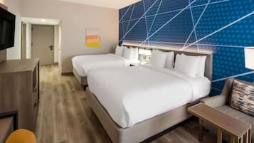 A hotel room with two beds, a desk, a TV, and a wall with a geometric pattern.