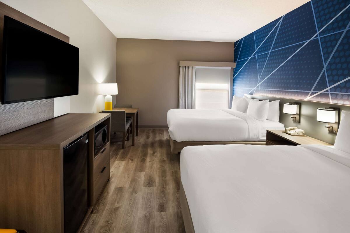 Habitación de hotel con dos camas, televisión, escritorio con lámpara y baño.