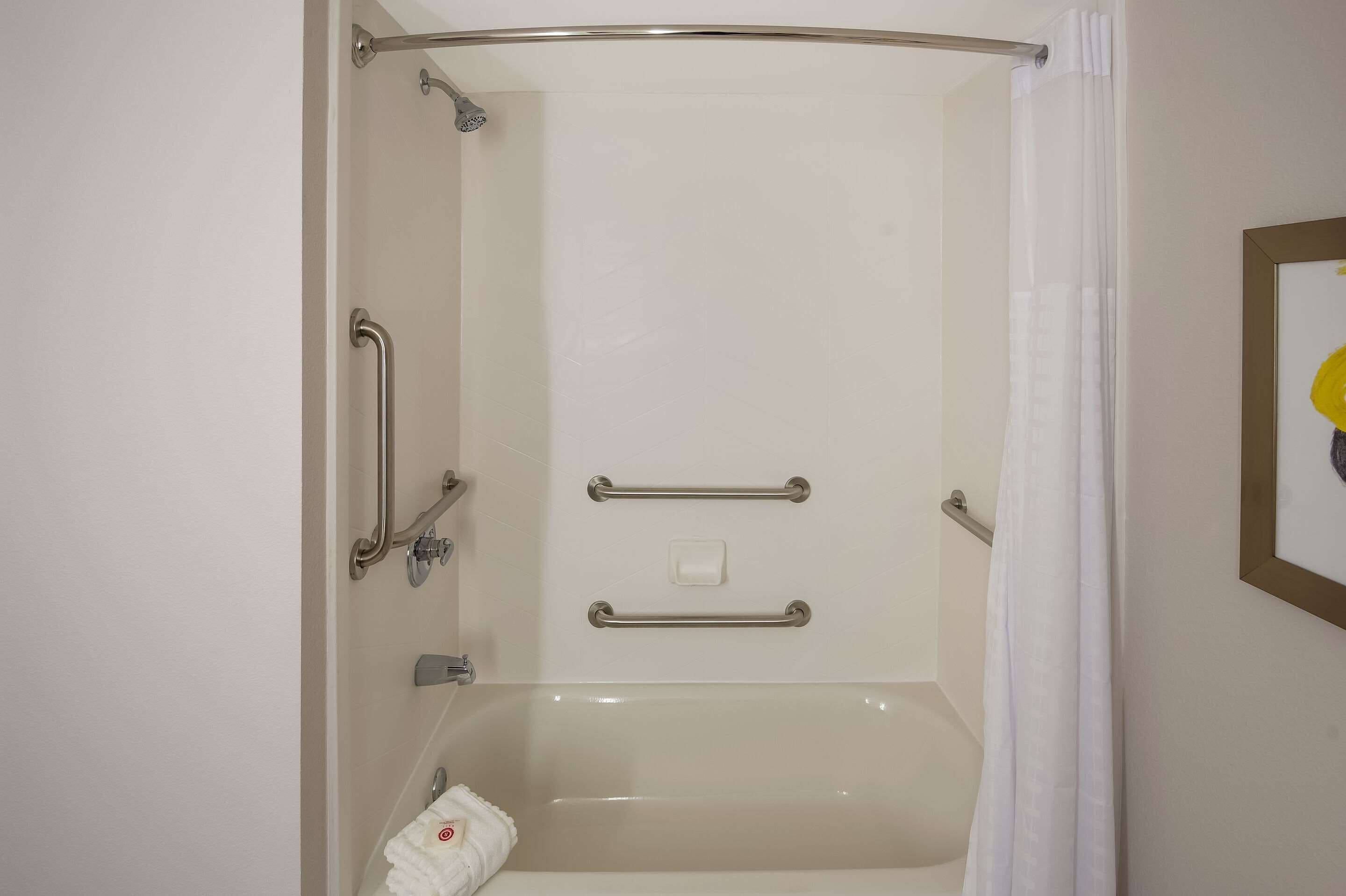 A bathroom with a bathtub, a shower with a glass door, and a handrail.