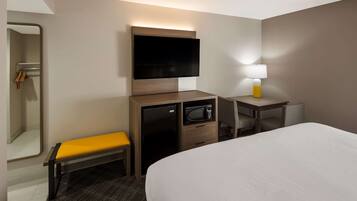 Une chambre d’hôtel comprenant un lit, un bureau avec une lampe, un téléviseur fixé au mur, un four à micro-ondes, un petit réfrigérateur et un banc.