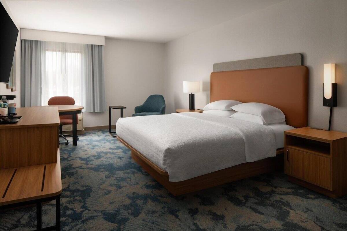 A hotel room with a bed, a desk, a chair, a lamp, and a TV.