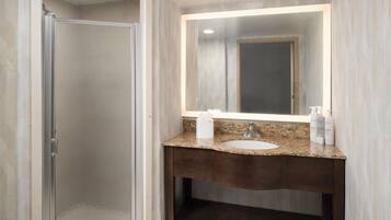 A bathroom with a glass shower enclosure, a granite countertop sink, and a mirror with built-in lighting.