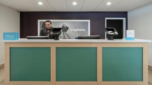 Ein Hotelrezeptionstresen mit einem digitalen Kiosk, einem gerahmten Bild und einem Schild für Hilton Honors.