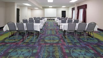 A conference room with rows of tables and chairs, a projector screen, and a carpeted floor.