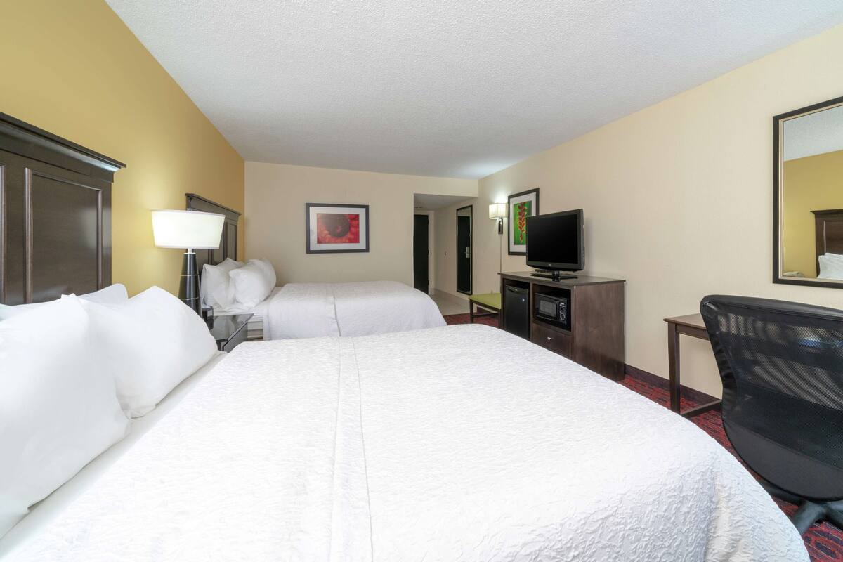 A hotel room with two beds, a television, a desk, and a chair.