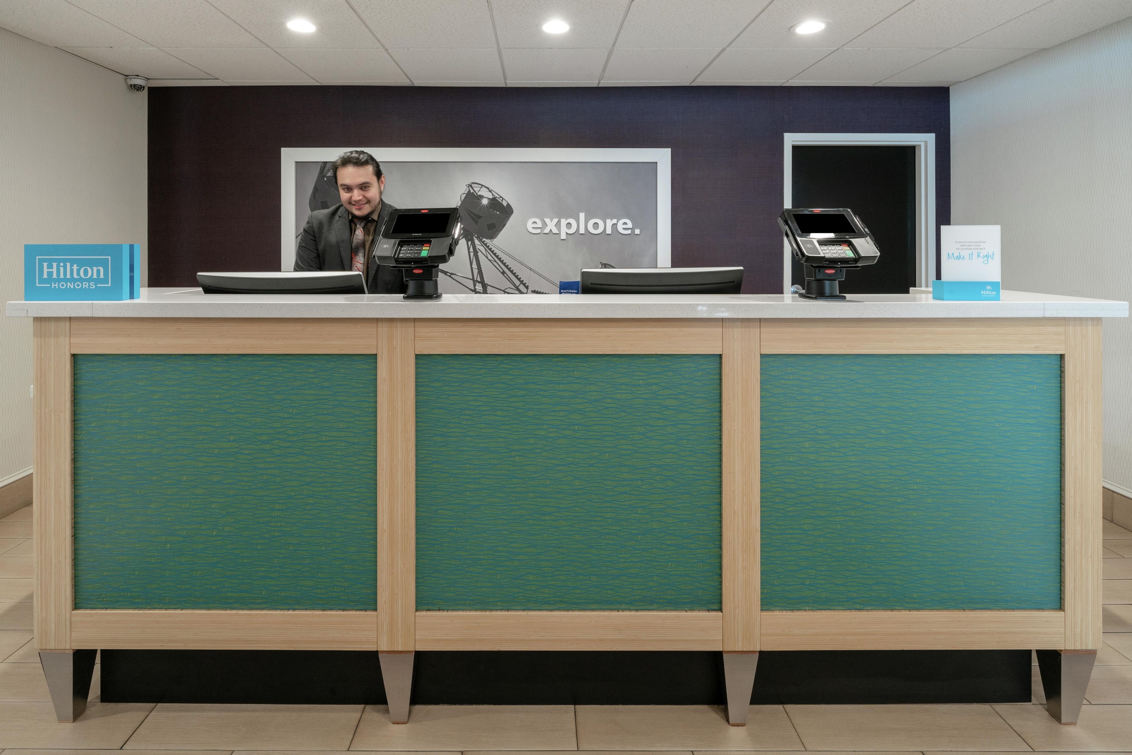 A hotel reception desk with a digital kiosk, a framed picture, and a sign for Hilton Honors.