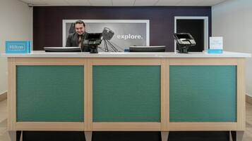A hotel reception desk with a digital kiosk, a framed picture, and a sign for Hilton Honors.