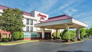 Ein Hampton Inn Hotel mit blauem Himmel, überdachtem Parkplatz und gepflegter Bepflanzung.
