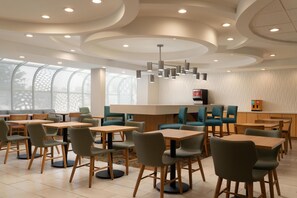 A modern dining area with round tables and chairs, a central light fixture, and a view through large windows. - Hampton Inn by Hilton Hopewell Fort Lee (Hopewell)